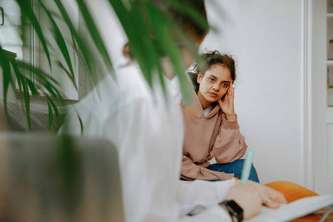 Tânără gânditoare așezată pe canapea, lângă o fereastră cu plante